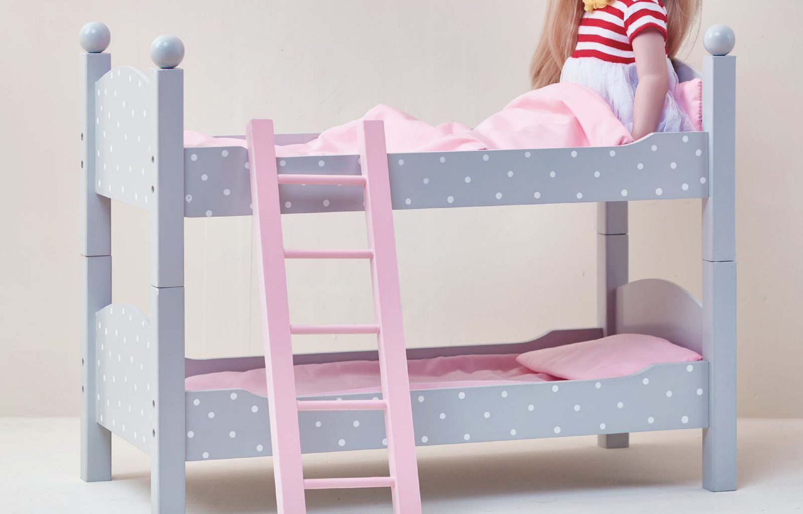 18-inch doll sitting on a wooden bunk bed with polka dot bedding
